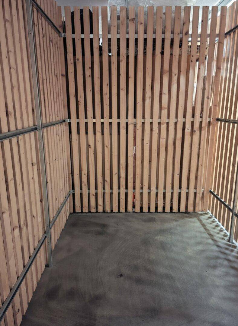 Geräumiger Abstellraum mit Holzlattenwänden und Betonboden, ideal für zusätzlichen Stauraum.