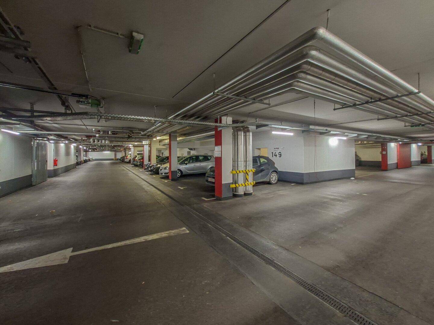 Weitläufige Tiefgarage mit zahlreichen Stellplätzen und sichtbaren Versorgungsleitungen an der Decke.