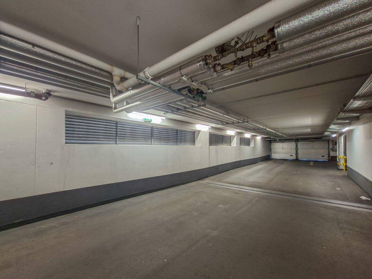 Tiefgaragenausfahrt mit Rolltoren und sichtbaren Lüftungsrohren an der Decke.