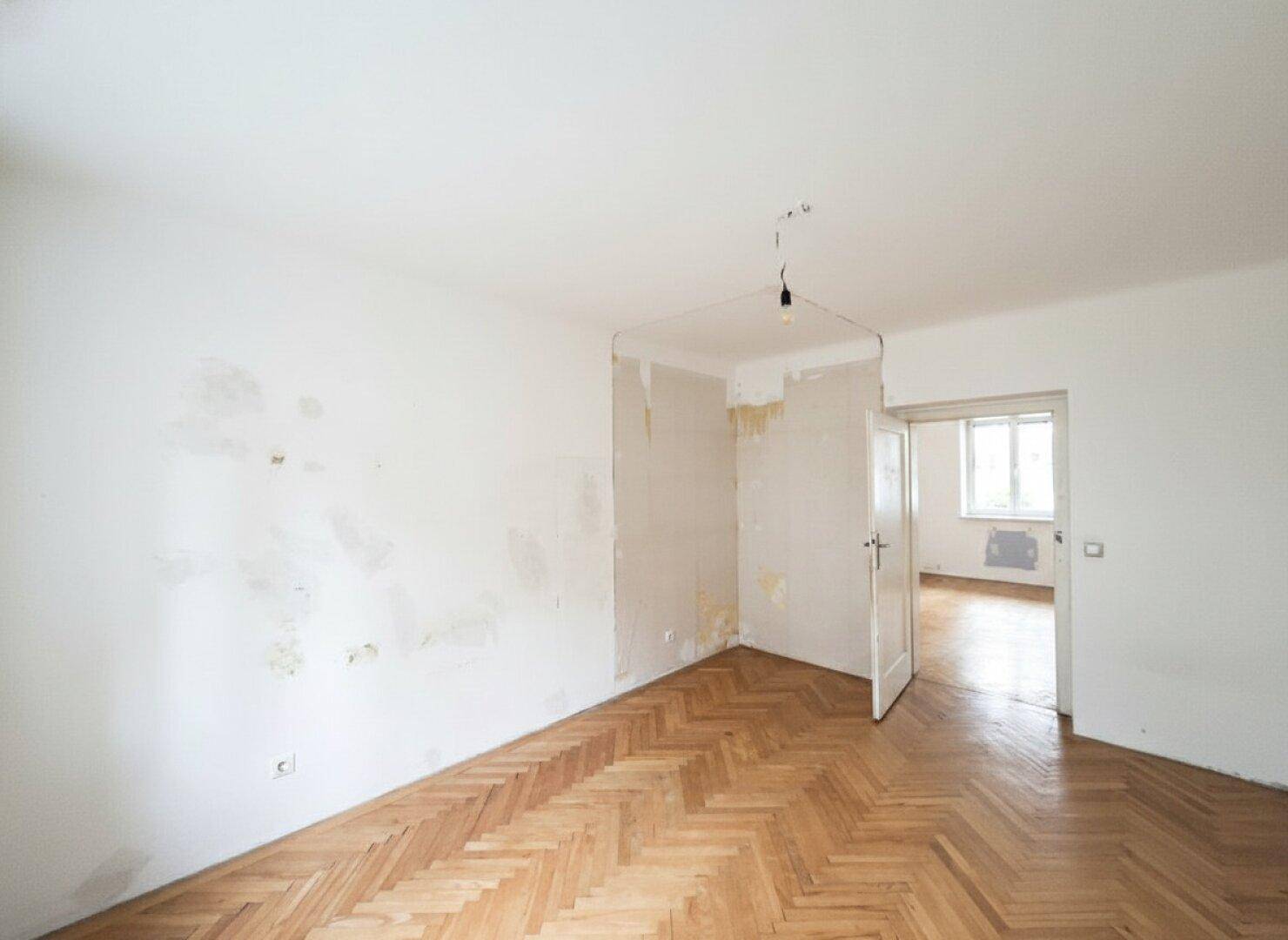Leerer Raum mit Fischgrätparkett und sichtbaren Spuren früherer Tapeten.