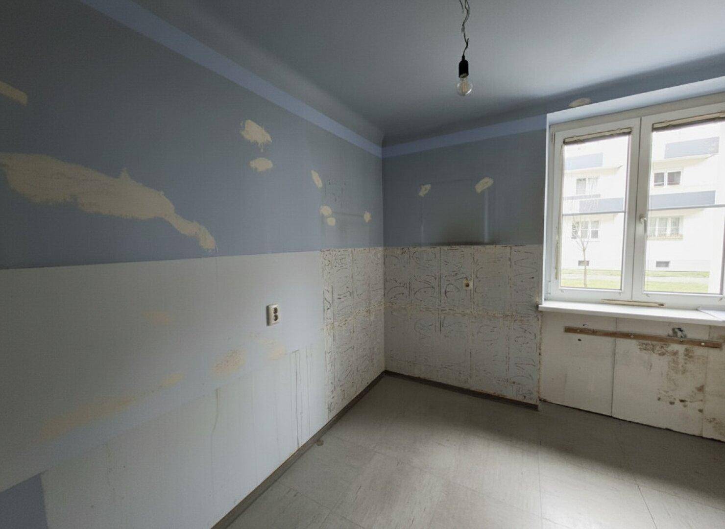 Renovierungsbedürftige Küche mit blauen Wänden und einem Fenster.