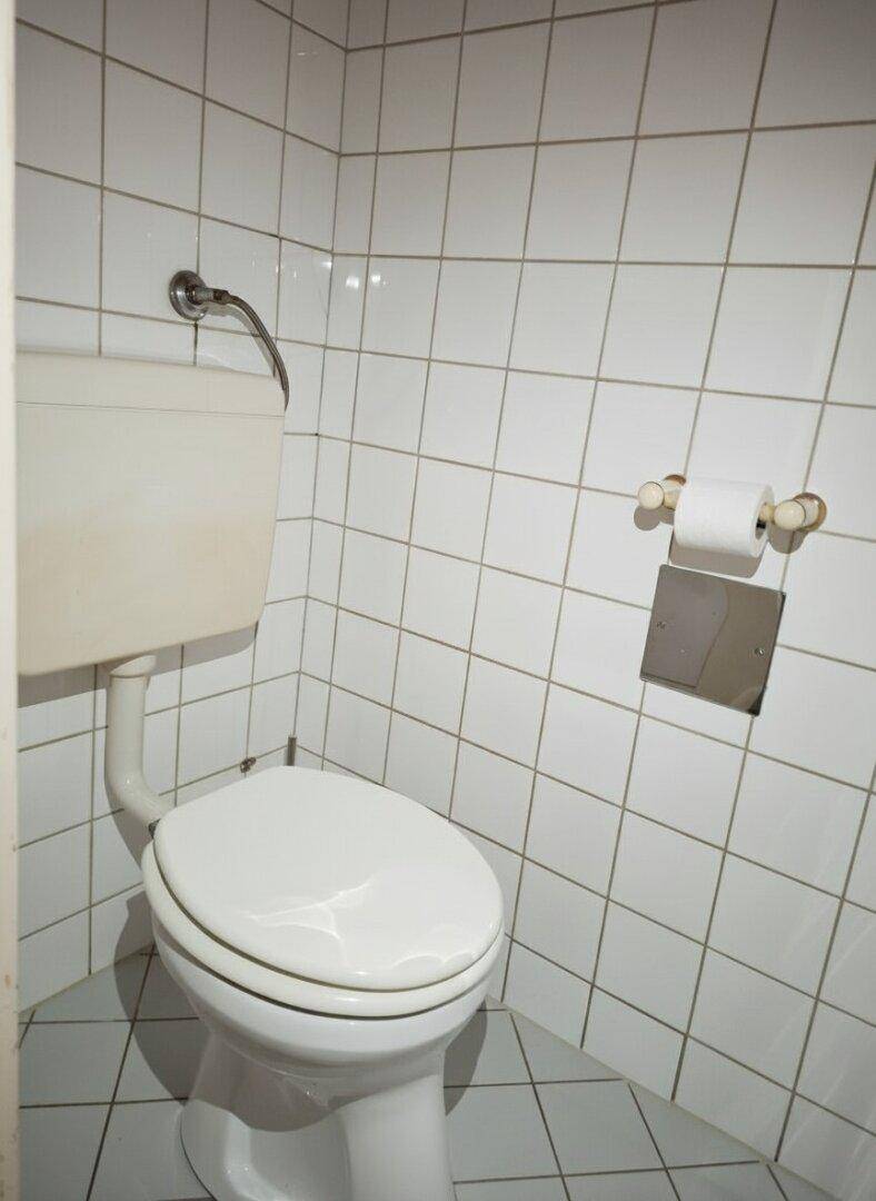 Toilette mit Spülkasten und weißen Wandfliesen in einem Badezimmer.