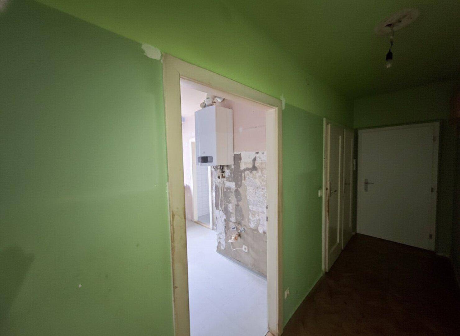 Grüner Flur mit Blick in einen Raum mit Gastherme, deutet auf Renovierungsbedarf hin.