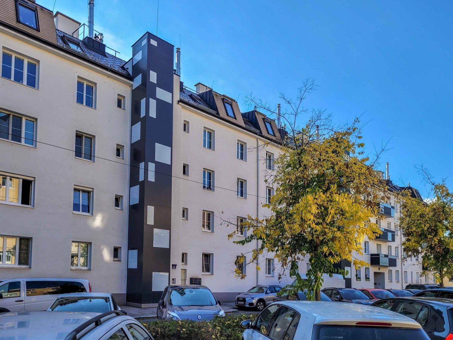 Außenansicht eines Wohngebäudes mit modernem Aufzugsschacht und Bäumen.