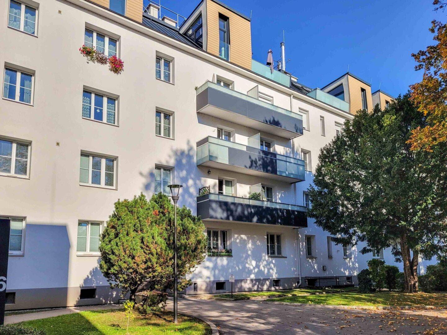 Wohngebäude mit mehreren Balkonen und großen Fenstern, umgeben von Grünflächen.