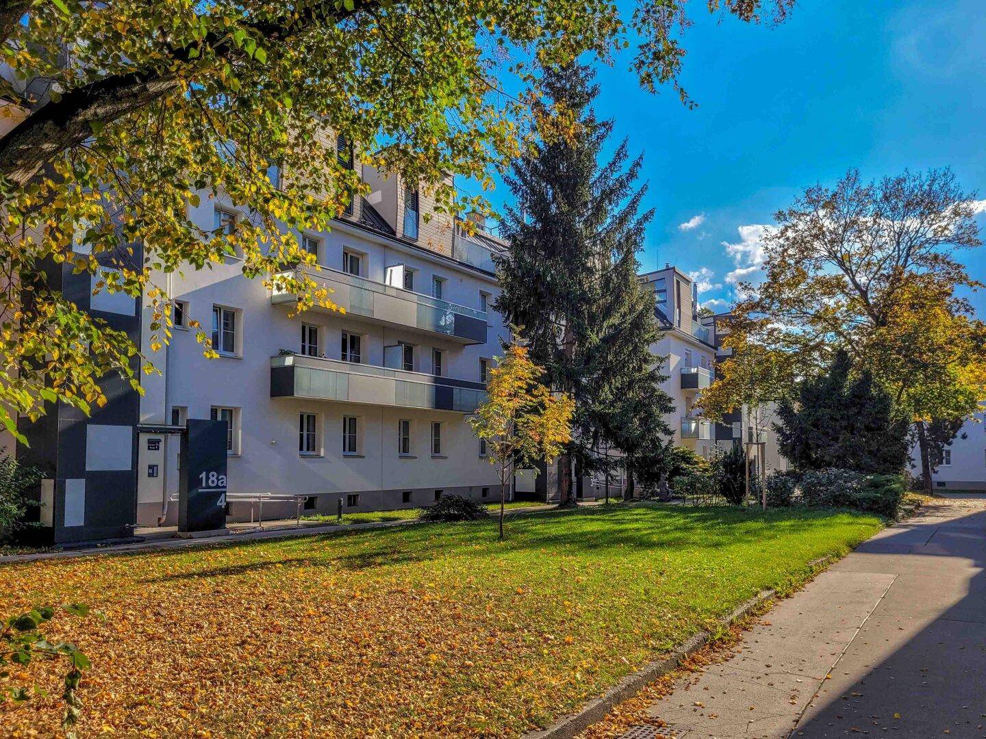 Wohngebäude umgeben von einer weitläufigen Grünfläche mit Bäumen und Wegen.