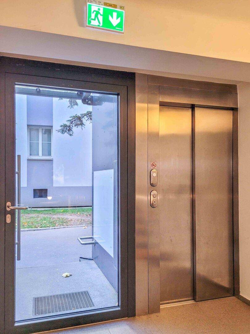Eingangsbereich eines Wohngebäudes mit modernem Aufzug und Glastür.