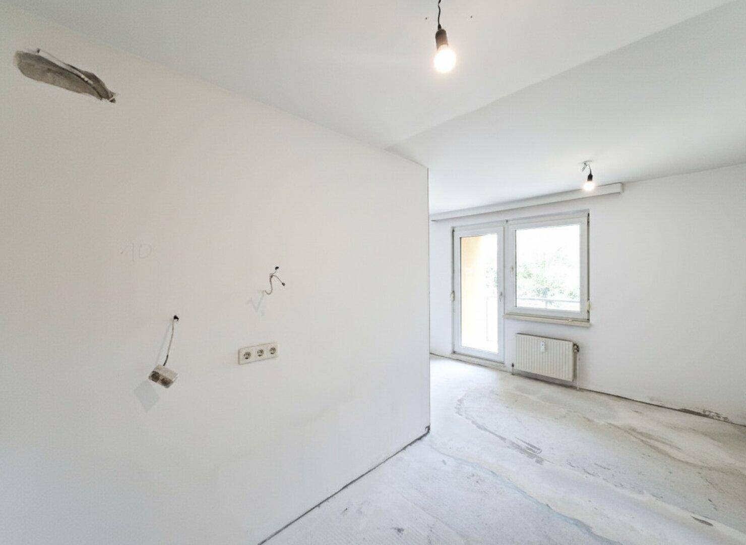 Unmöblierter Raum mit Estrichboden, elektrischen Anschlüssen und Fenster zum Außenbereich.