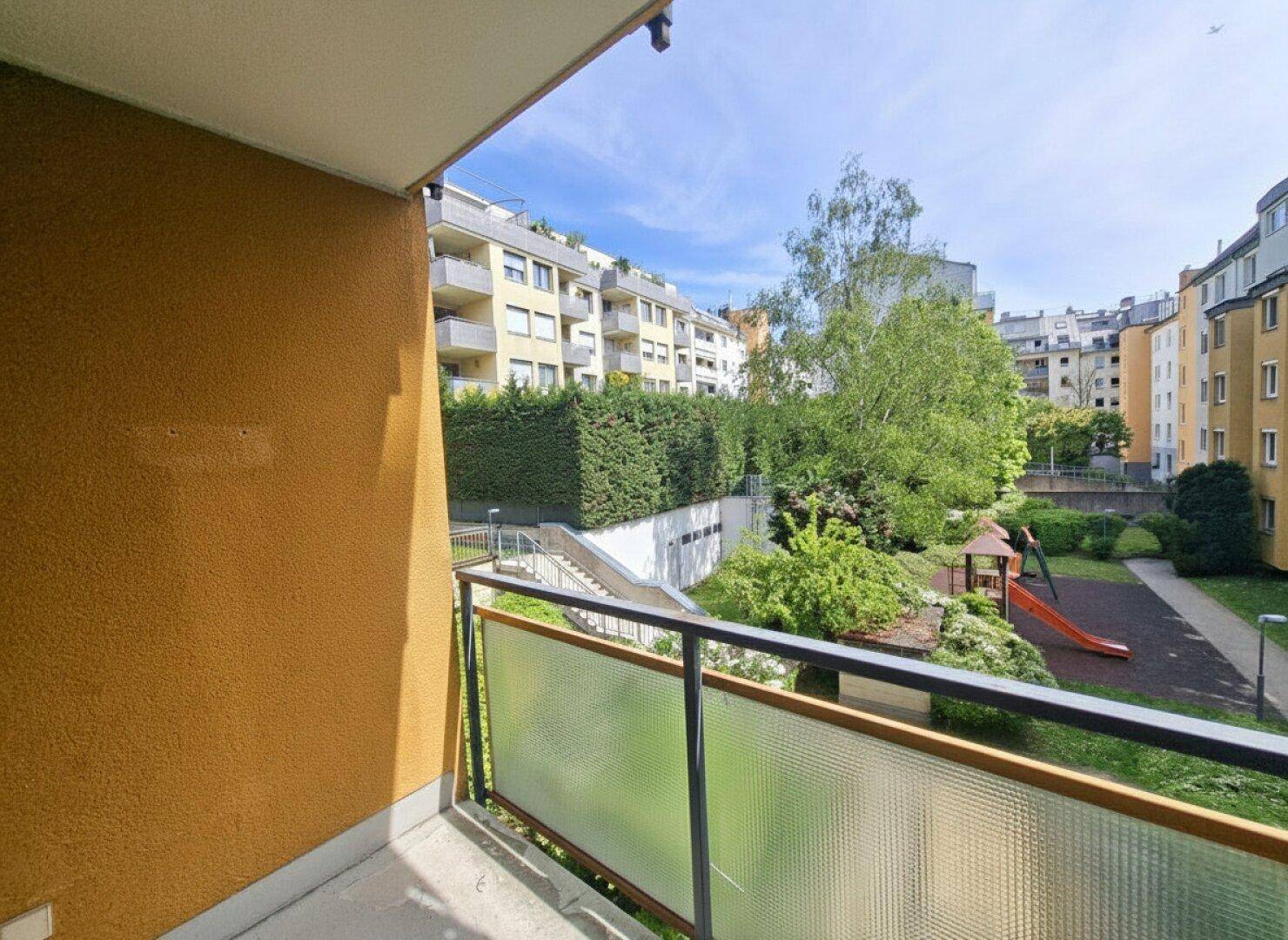 Balkon mit Aussicht auf den begrünten Innenhof und die umliegenden Gebäude.