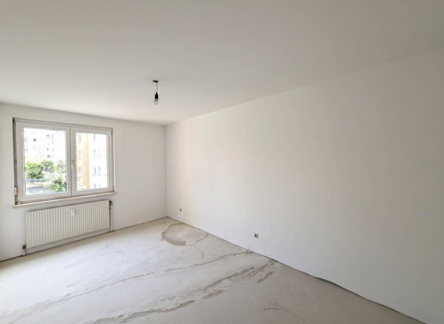 Helles, unmöbliertes Schlafzimmer mit Estrichboden und großem Fenster.