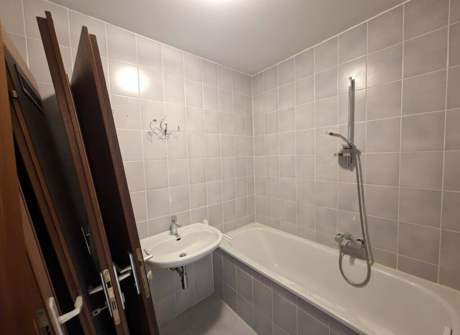 Badezimmer mit Badewanne, Waschbecken und hellgrauen Fliesen an den Wänden.
