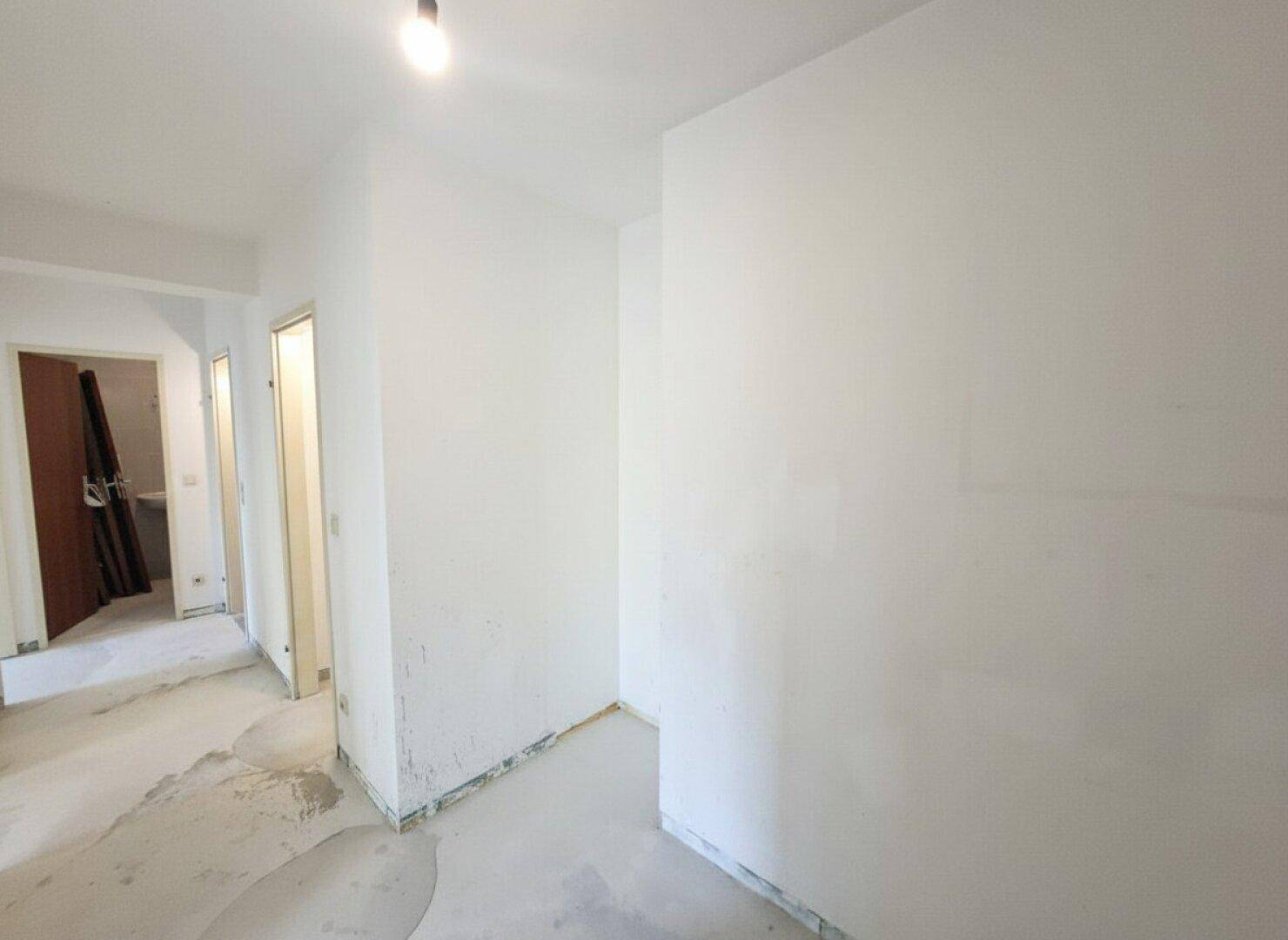 Heller Flur mit Estrichboden und Zugang zu verschiedenen Räumen der Wohnung.