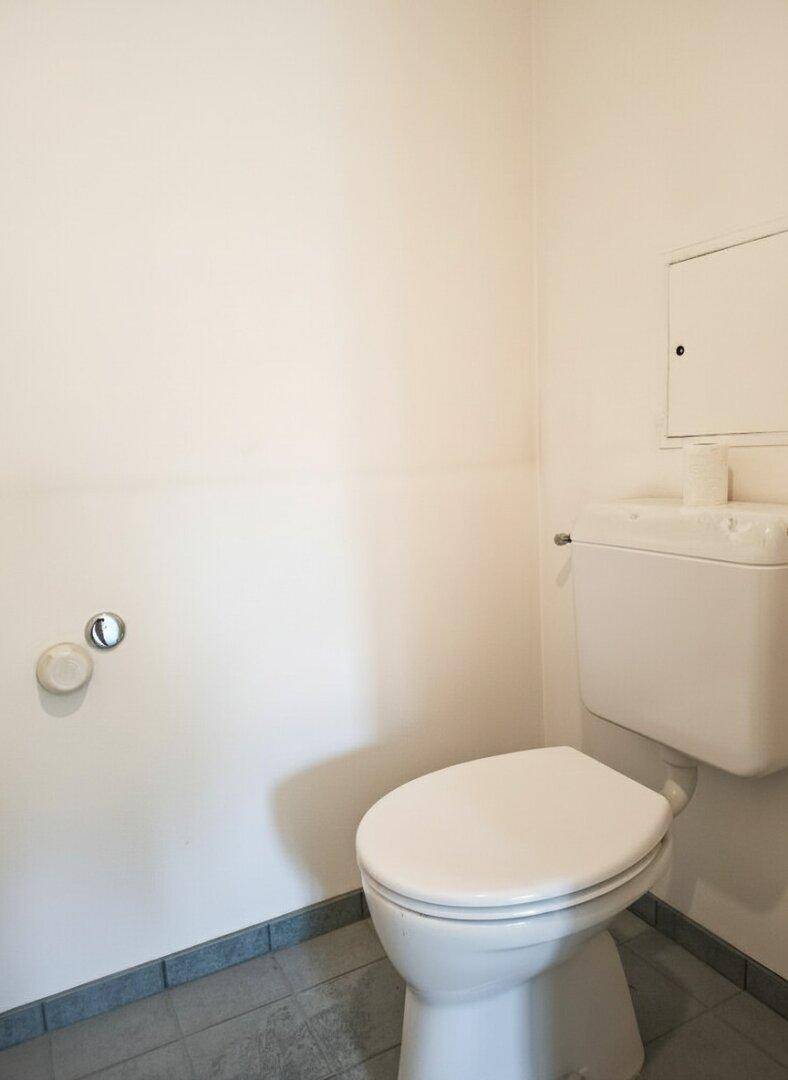 Einfaches WC mit Standtoilette und Fliesenboden, in einem kleinen Raum.