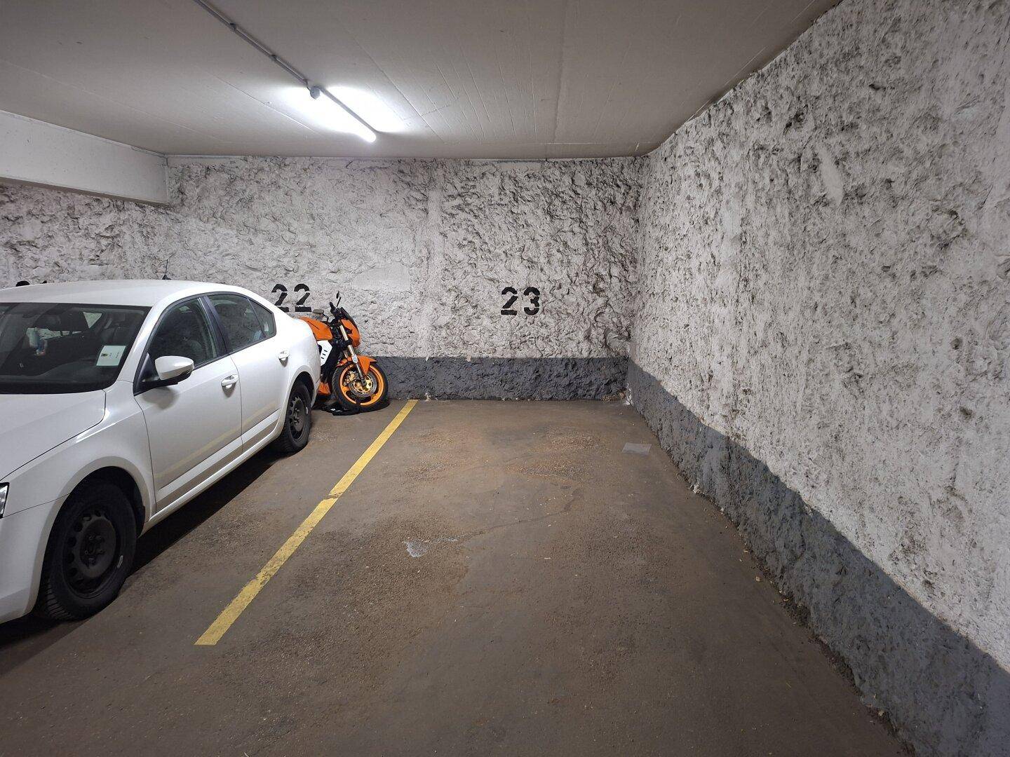 Einzelner Stellplatz in einer Tiefgarage mit rauen Betonwänden.