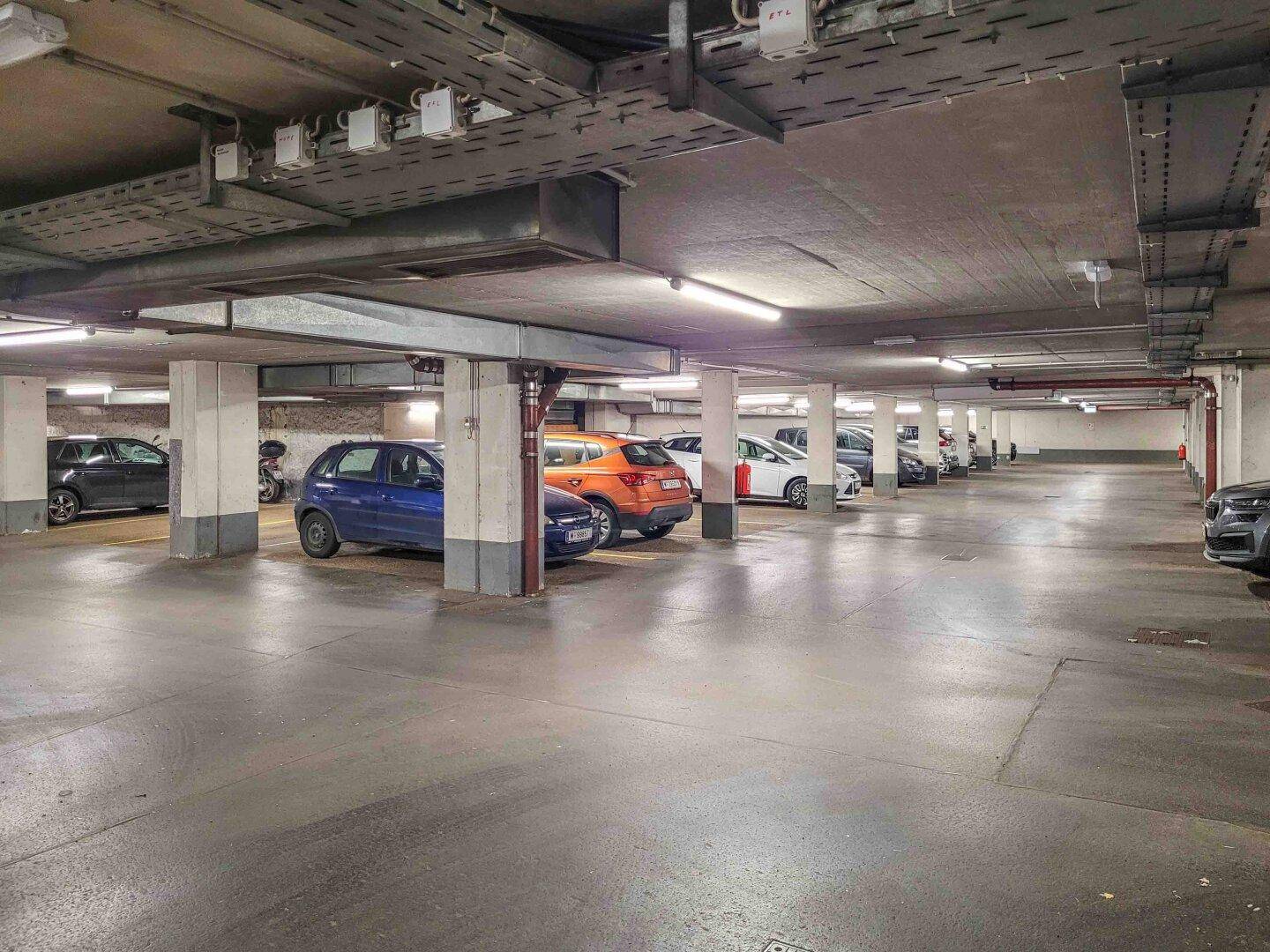 Geräumige Tiefgarage mit mehreren Stellplätzen und sichtbaren Installationen an der Decke.