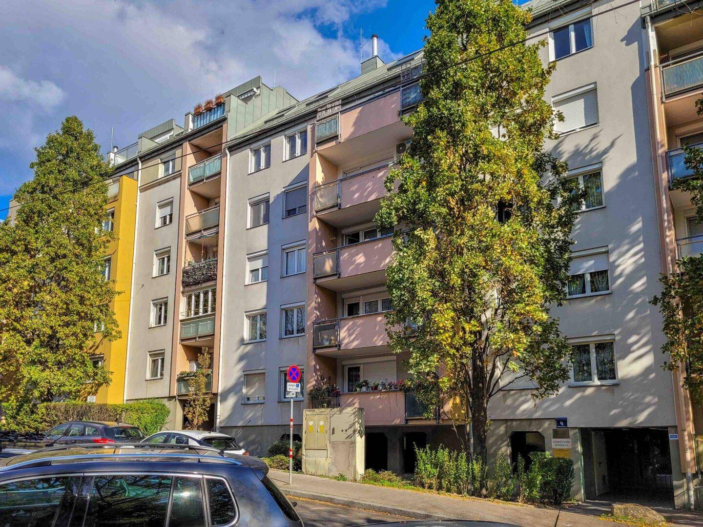 Mehrfamilienhaus mit farbiger Fassade, Balkonen und Bäumen im Vordergrund.