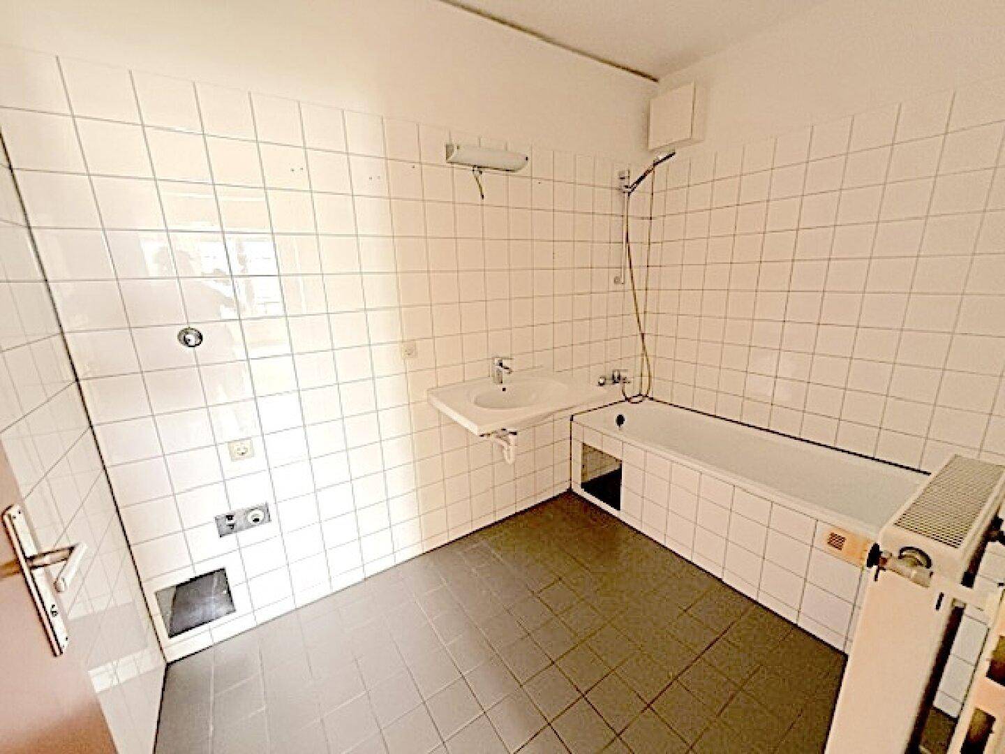 Funktionales Badezimmer mit weißen Wandfliesen, Badewanne und Waschbecken.