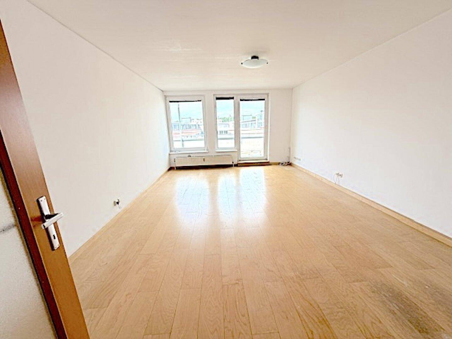 Lichtdurchfluteter Raum mit hellem Parkettboden und Zugang zur Terrasse durch große Fenster.