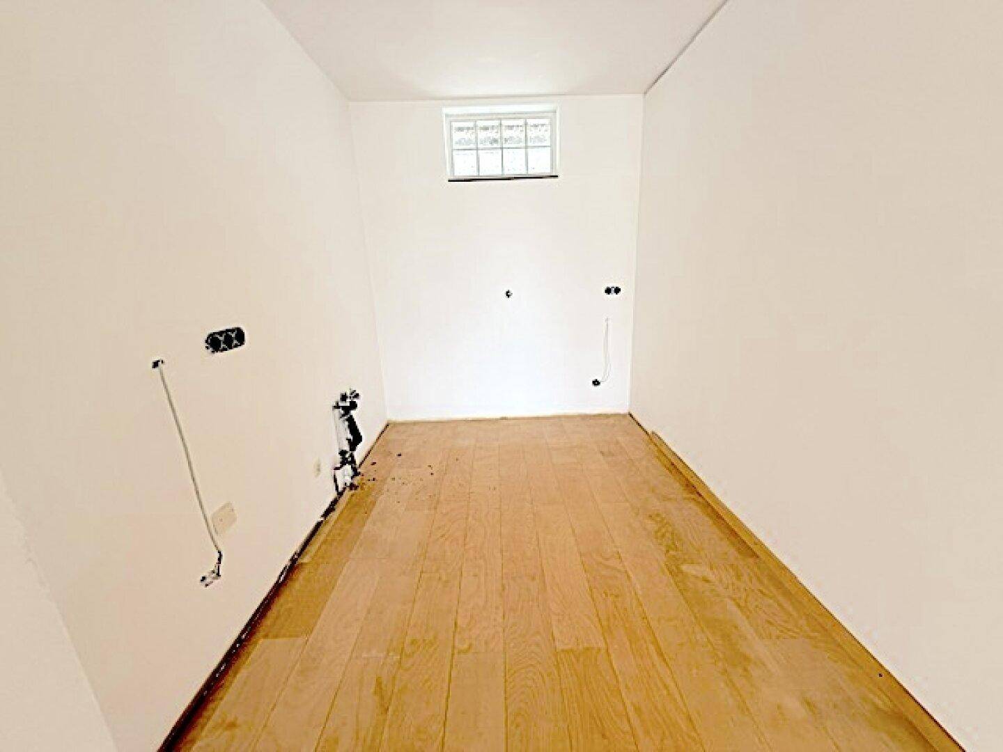 Leerer Raum mit Parkettboden und kleinem Fenster, ideal als Abstellraum oder Hauswirtschaftsraum.