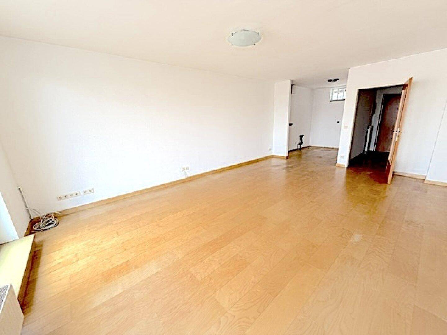 Heller Wohnbereich mit Parkettboden und offenem Übergang zu einem weiteren Raum.