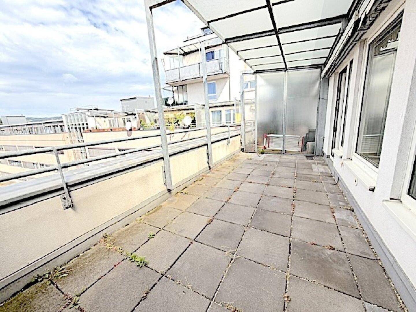 Weitläufige Terrasse mit Fliesenboden und Überdachung, umgeben von urbaner Architektur.