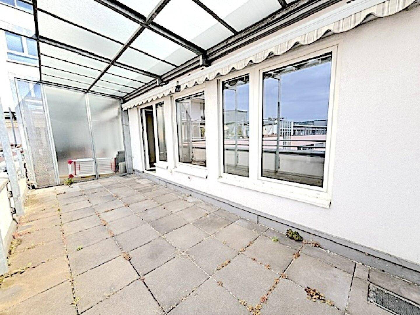 Überdachte Terrasse mit Fliesenboden und großen Fenstern, die viel Licht in die Innenräume lassen.