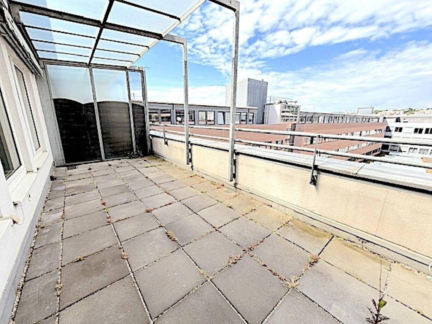 Geräumige Dachterrasse mit Fliesenboden und Überdachung, bietet einen weiten Blick über die Stadt.