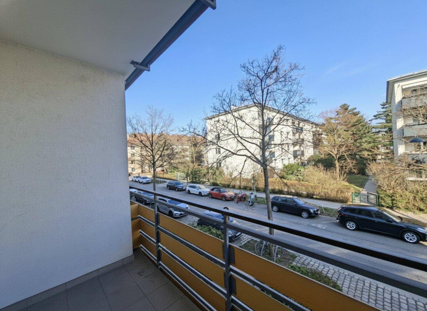 Blick vom Balkon auf die Straße mit parkenden Autos und umliegenden Gebäuden.
