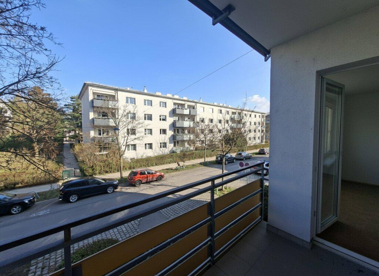 Blick vom Balkon auf eine Wohnstraße mit gegenüberliegendem Mehrfamilienhaus und Balkonen.