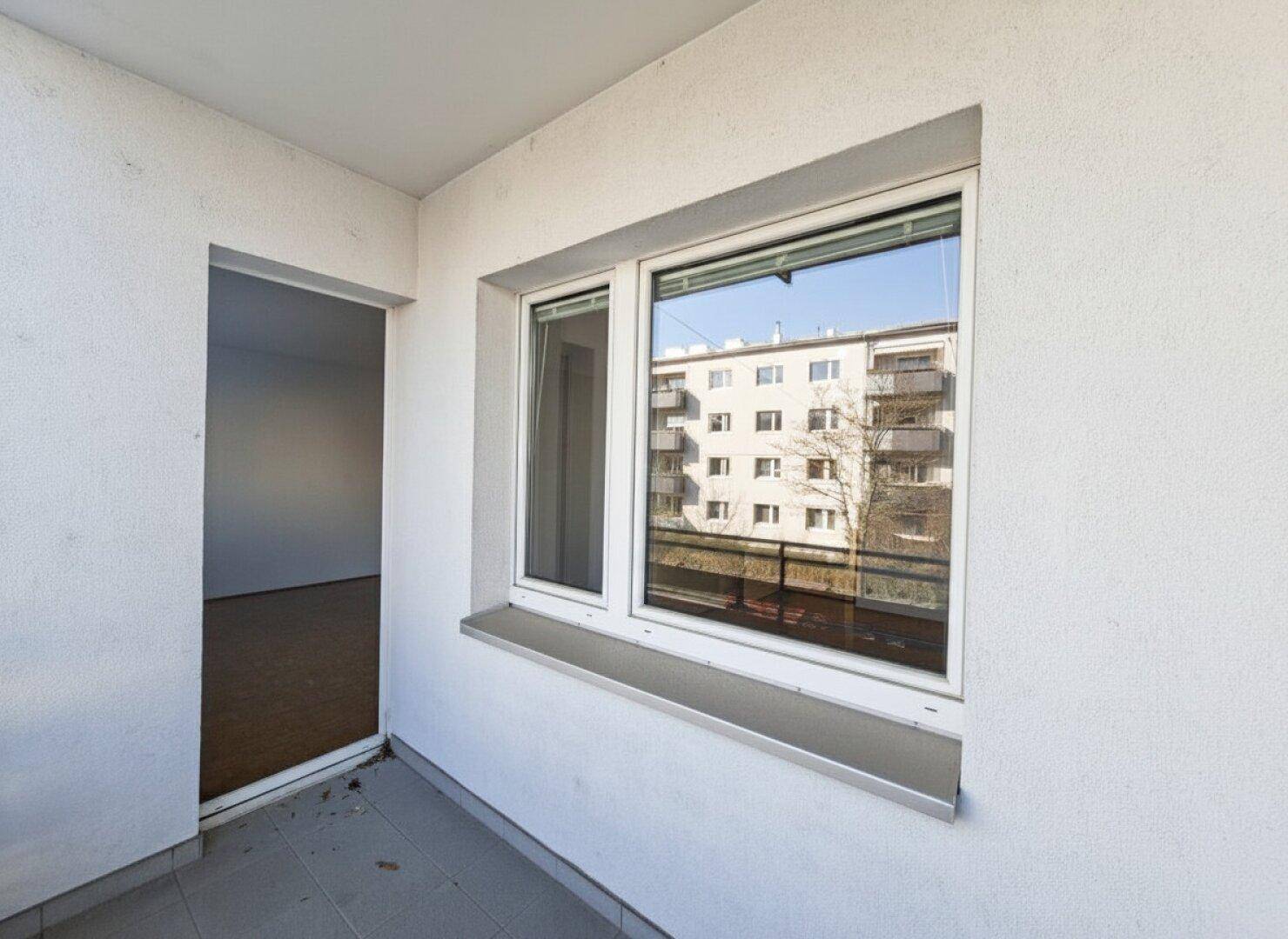 Innenansicht eines Balkons mit Fenster, das das gegenüberliegende Gebäude widerspiegelt.