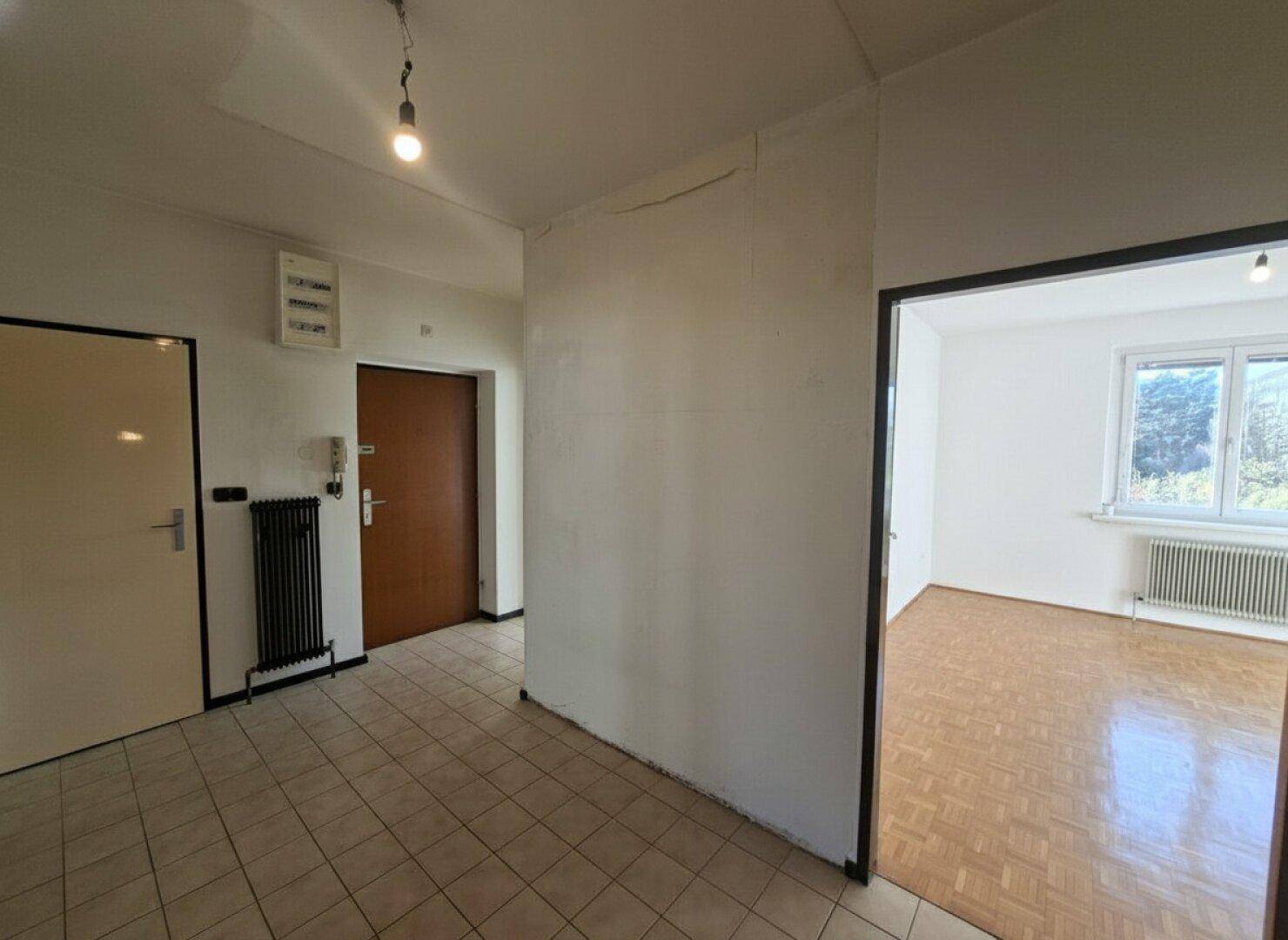 Eingangsbereich mit Fliesenboden, weißer Wand, Haustür und einem Heizkörper.