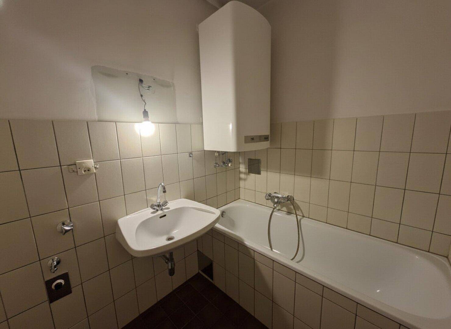Badezimmer im älteren Stil mit Badewanne, Waschbecken und hellen Fliesen an den Wänden.