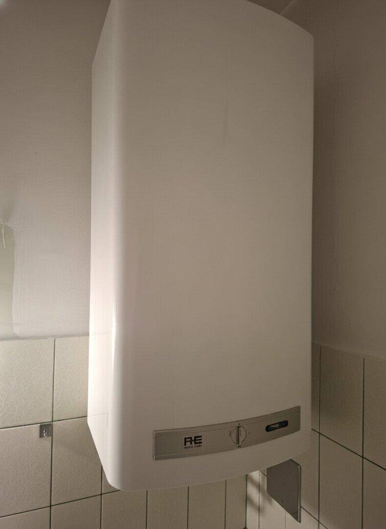 Nahaufnahme eines Warmwasserboilers an der Wand in einem gefliesten Badezimmer.