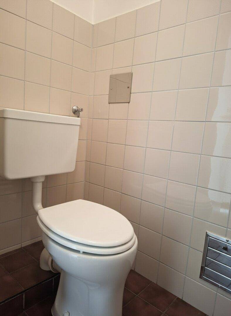 Separate Toilette mit Stand-WC und hellen Fliesen an den Wänden.