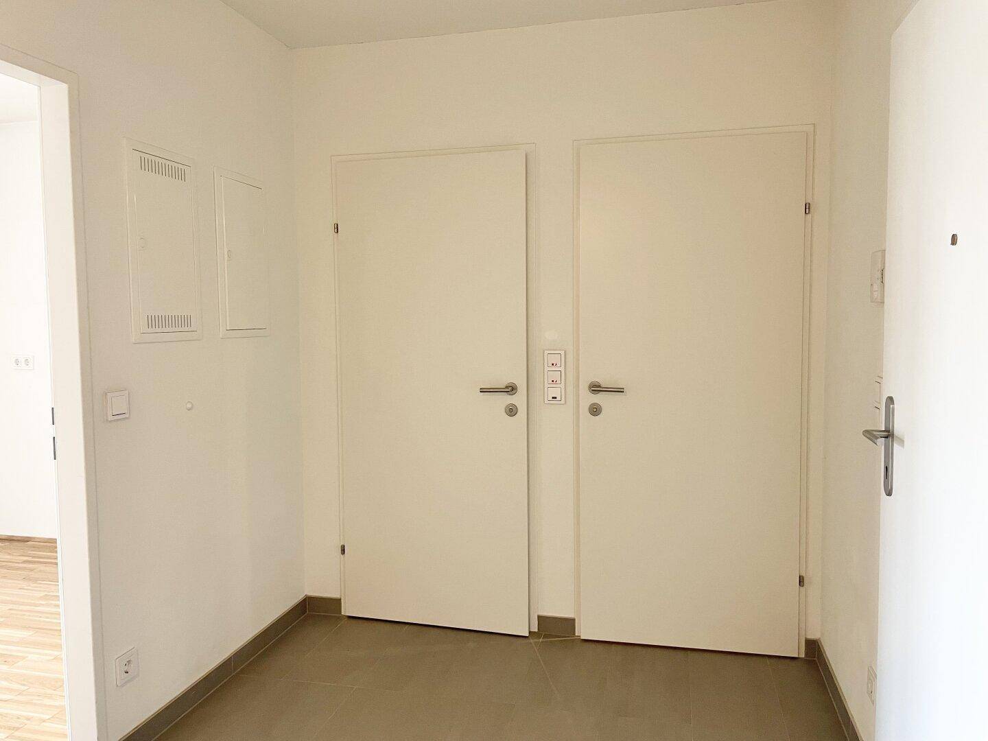 Heller Eingangsbereich mit Fliesenboden und mehreren weißen Türen.