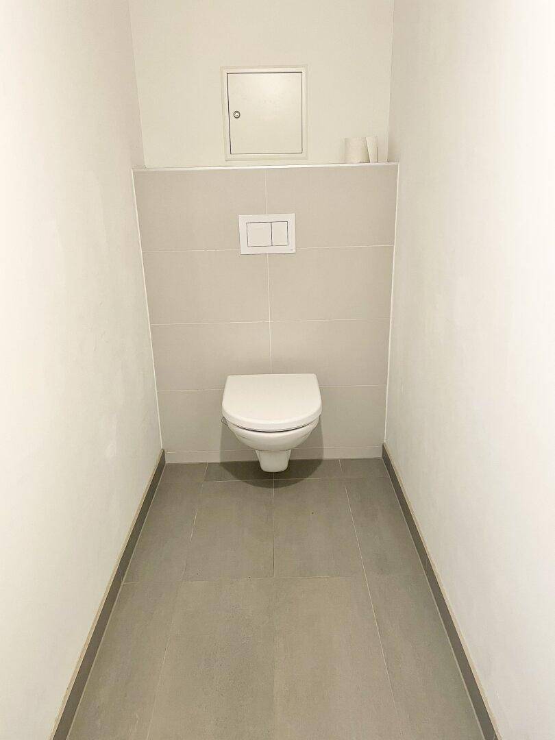 Separates WC mit wandhängender Toilette und modernen grauen Fliesen.