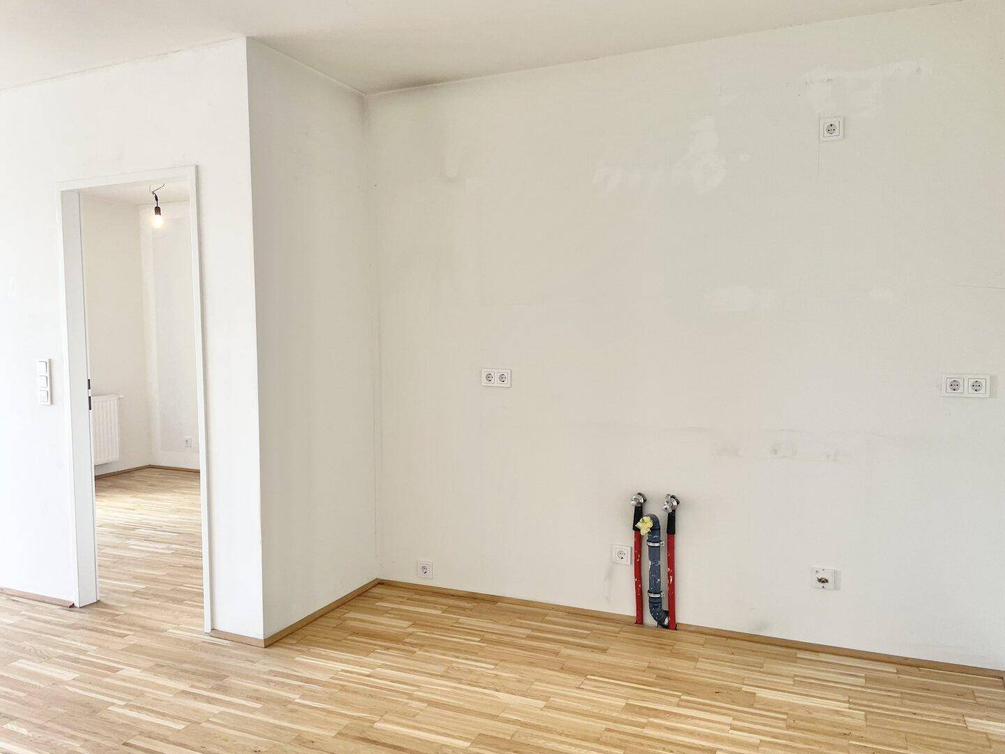 Heller Wohnbereich mit Parkettboden und Anschlüssen für eine zukünftige Küche.