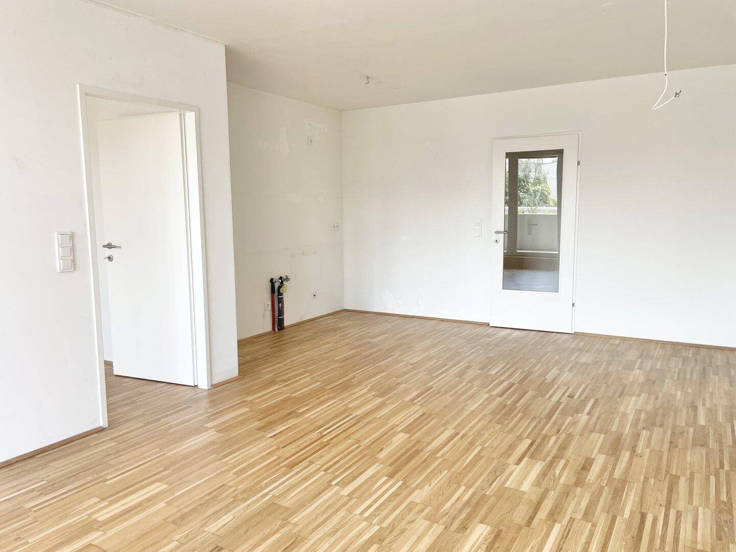 Geräumiger, heller Raum mit Parkettboden und weiß gestrichenen Wänden.