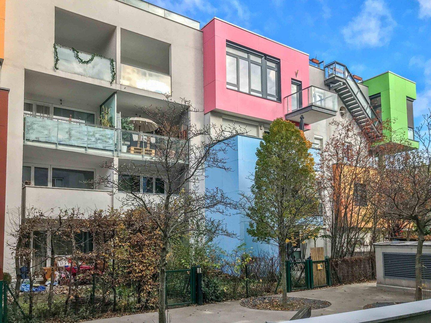Moderne Wohngebäude mit farbenfrohen Fassaden, Balkonen und Außentreppen unter blauem Himmel.