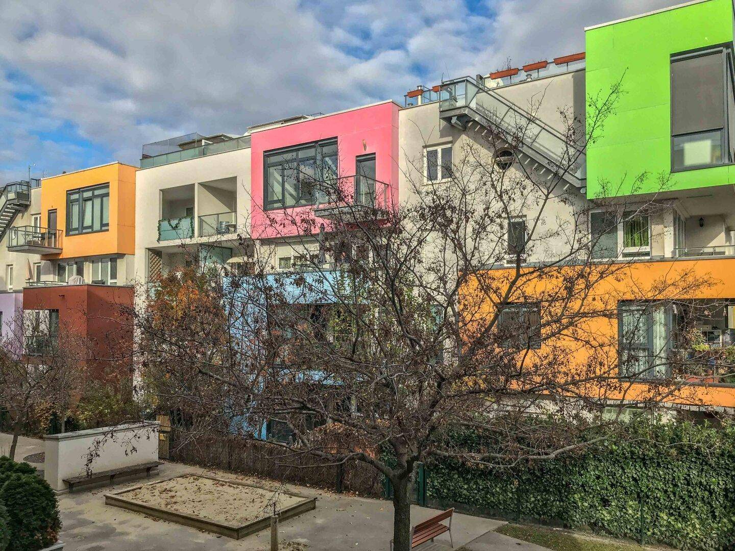 Bunte Wohnanlage mit modernen Fassaden, Balkonen und einem Sandkasten im Vordergrund.