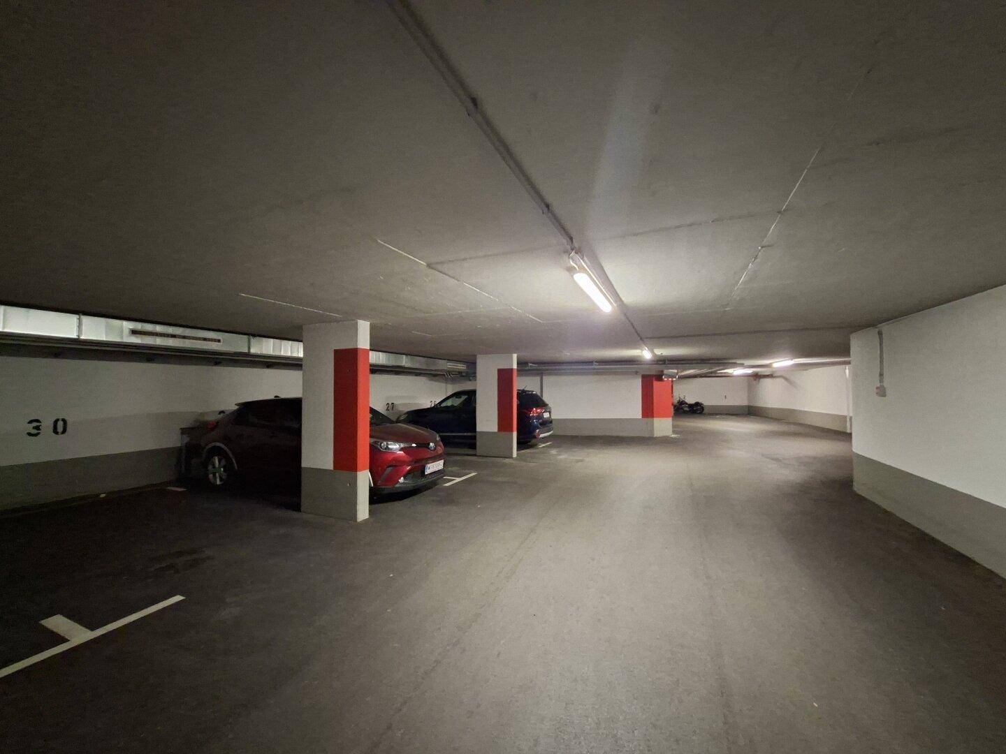 Tiefgarage mit einigen geparkten Autos, roten Säulen und heller Deckenbeleuchtung.