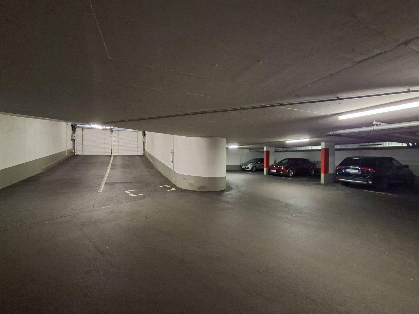 Einfahrt und Stellplätze in einer Tiefgarage mit heller Beleuchtung und Betonwänden.