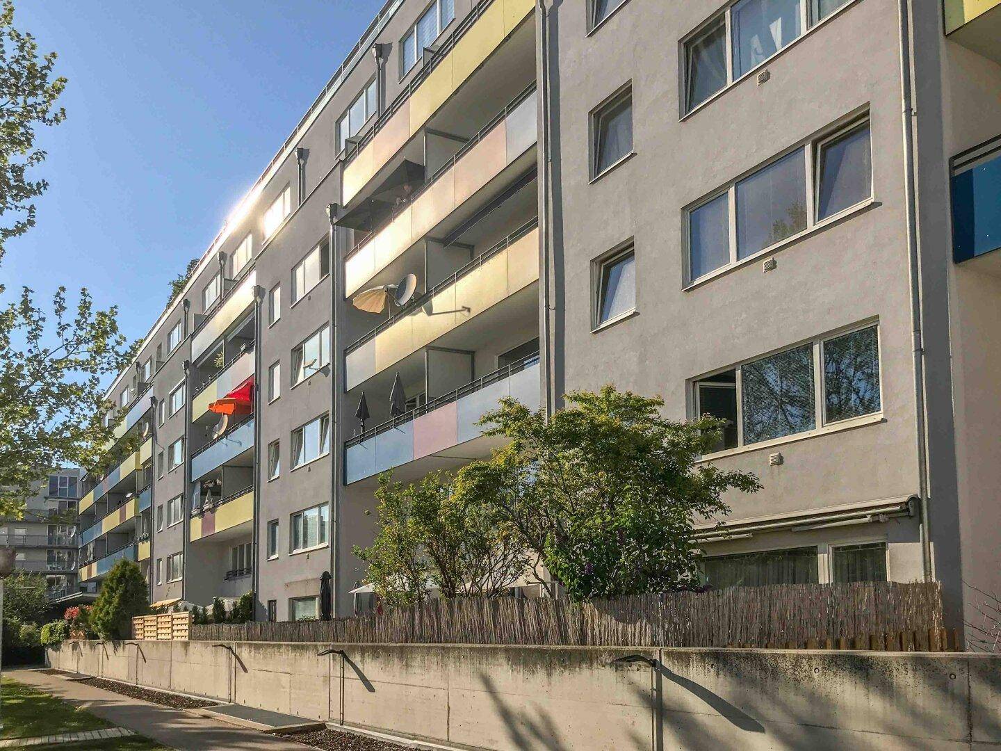 Moderne Wohnhausfassade mit vielen Balkonen und großen Fenstern unter strahlendem Sonnenschein.