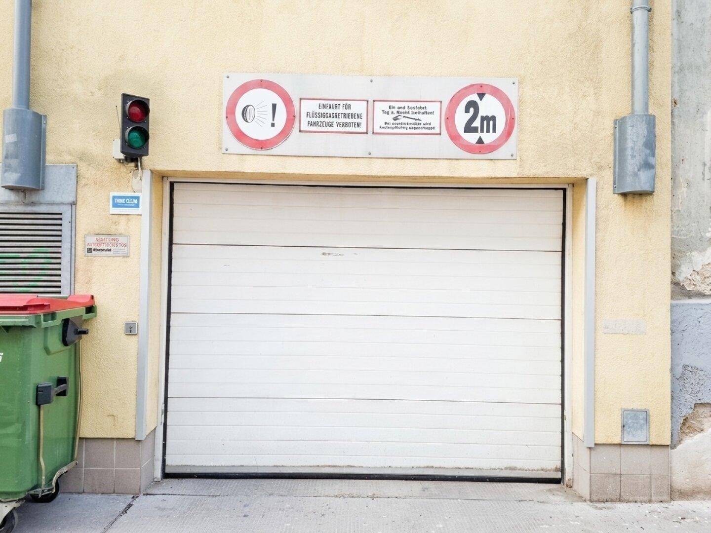 Garageneinfahrt mit weißem Rolltor, Ampel und Hinweisschildern zur Zufahrt.