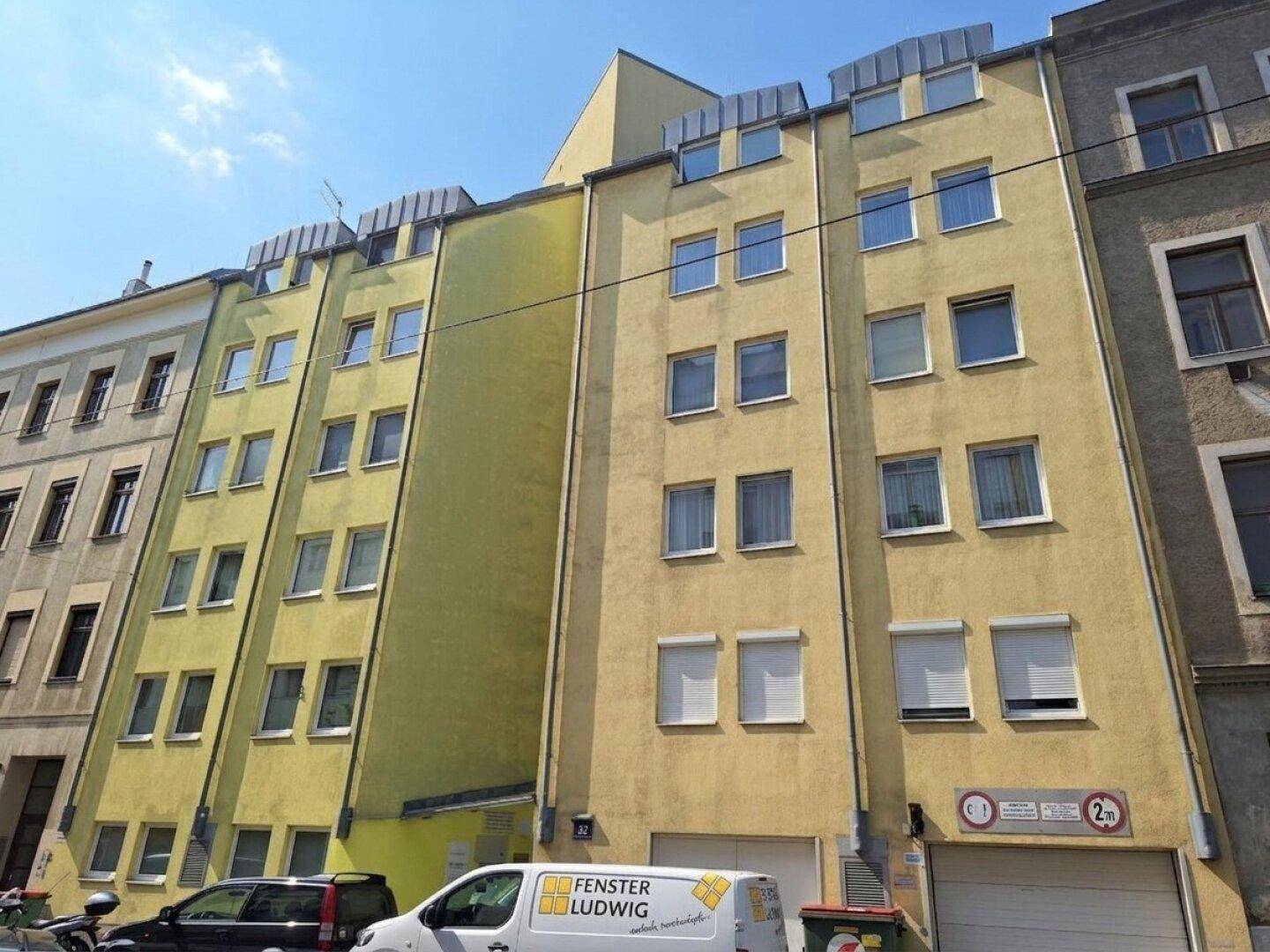 Mehrstöckiges Wohngebäude mit gelber Fassade, vielen Fenstern und Garageneinfahrt.