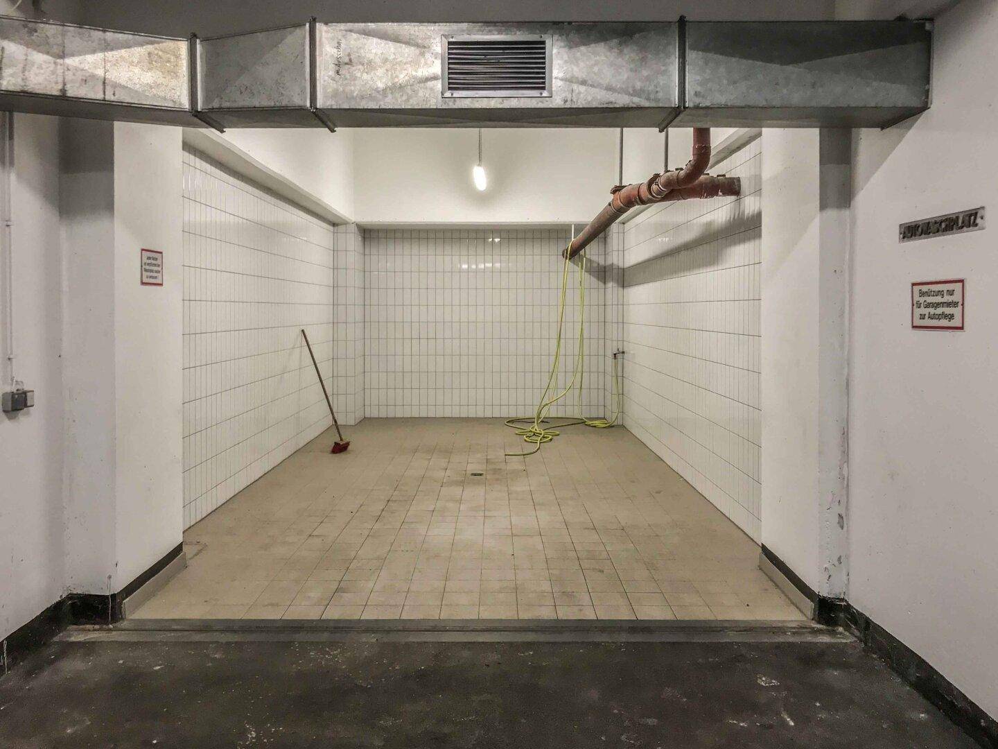 Gefliester Raum mit Schlauch und Besen, möglicherweise eine Waschbucht in der Tiefgarage.