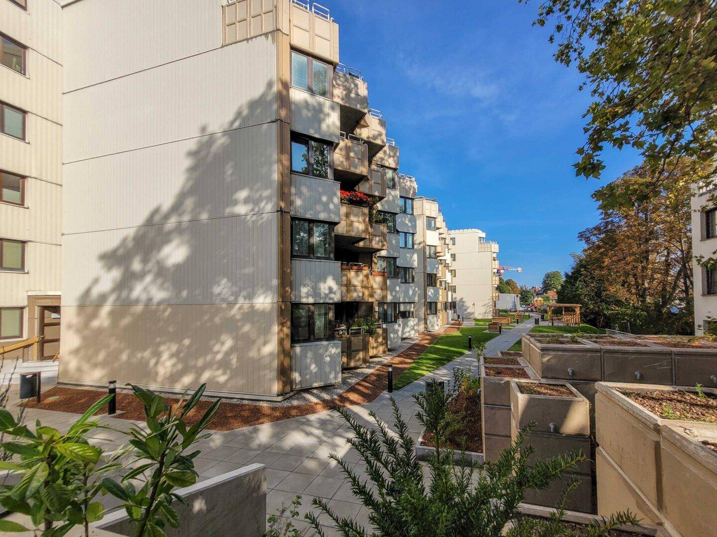 Seitenansicht des Apartmentgebäudes mit begrünten Außenbereichen und Pflanzkübeln.