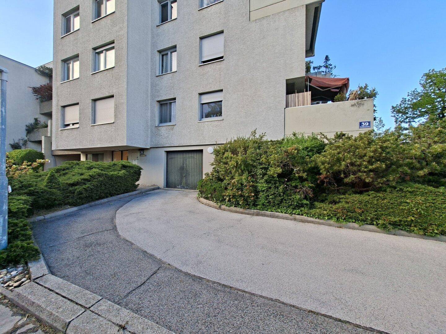Mehrfamilienhaus mit Garagenzufahrt und gepflegten Büschen im Vordergrund.