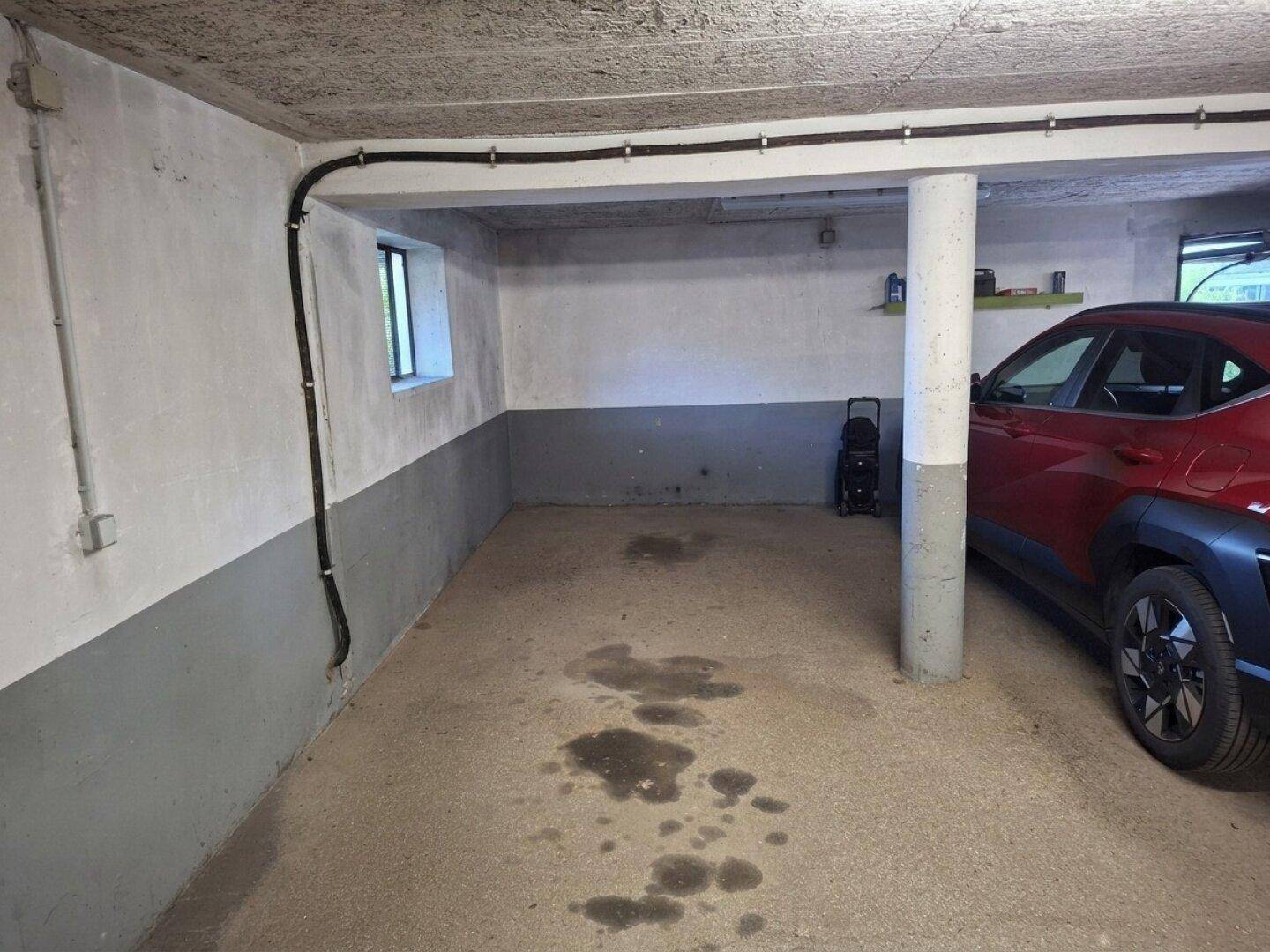 Ecke einer Tiefgarage mit einem Fahrzeug, sichtbaren Leitungen und einem kleinen Fenster.