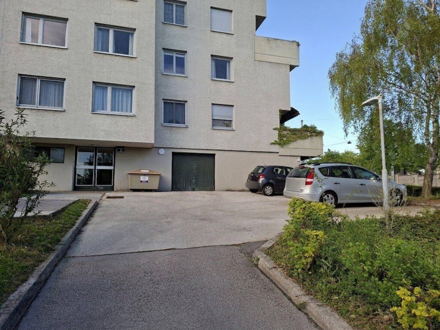 Wohngebäude mit Haupteingang, Garagentor und geparkten Autos auf dem Vorplatz.